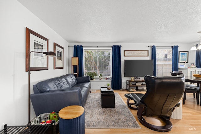 living room featuring light wood-style floors, a textured ceiling, and an inviting chandelier