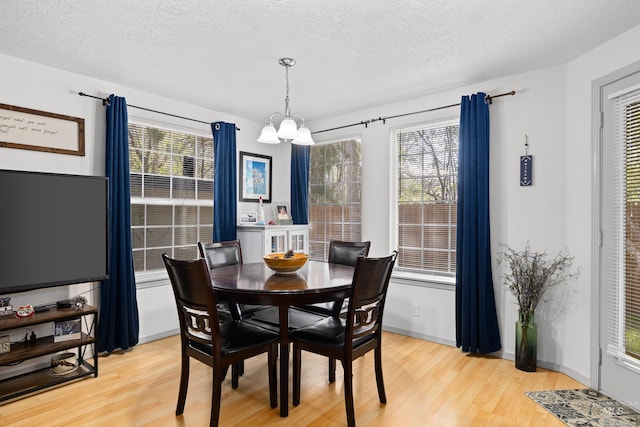 dining area with a notable chandelier, a healthy amount of sunlight, a textured ceiling, and light wood-style flooring