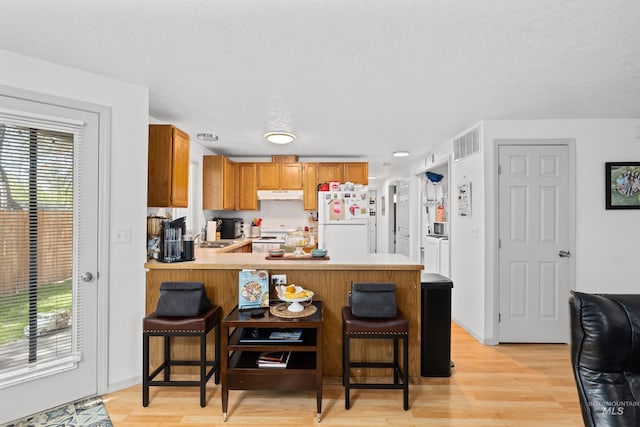 kitchen featuring under cabinet range hood, visible vents, white appliances, and plenty of natural light