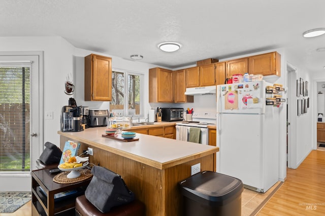 kitchen with a peninsula, plenty of natural light, under cabinet range hood, and white appliances