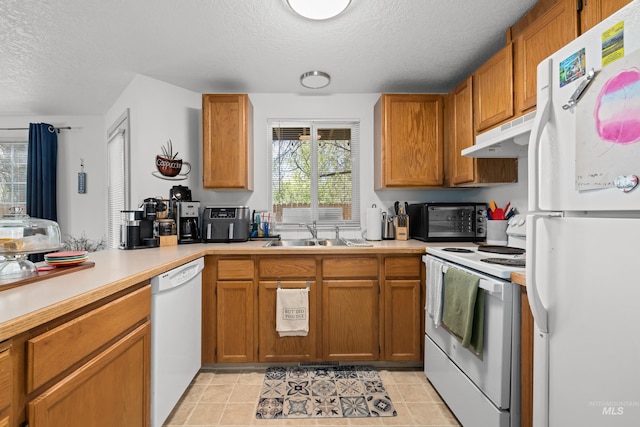 kitchen featuring a sink, a textured ceiling, white appliances, light countertops, and under cabinet range hood