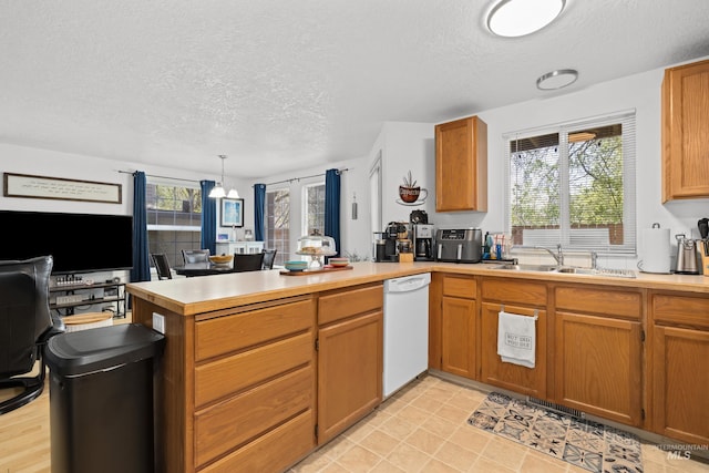 kitchen featuring a sink, a textured ceiling, dishwasher, light countertops, and a peninsula