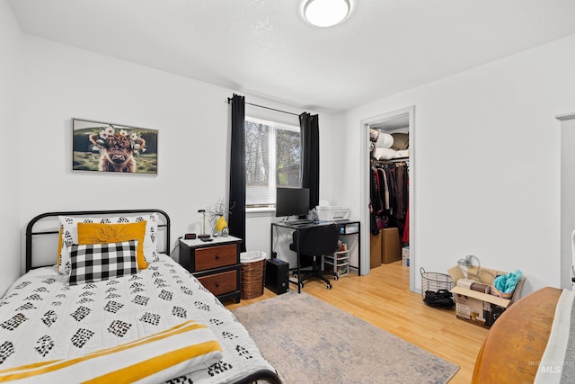bedroom with a walk in closet, wood finished floors, and a closet