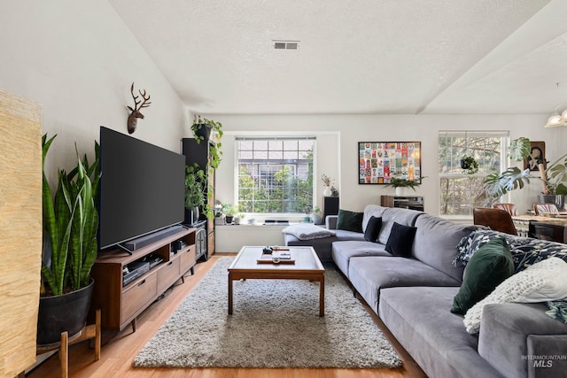 living room featuring a textured ceiling, light wood-type flooring, and visible vents