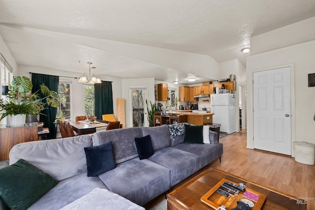living area featuring plenty of natural light, vaulted ceiling, a notable chandelier, and light wood-type flooring