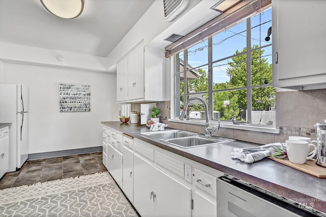 kitchen featuring a sink, stone finish flooring, stainless steel dishwasher, white cabinetry, and freestanding refrigerator