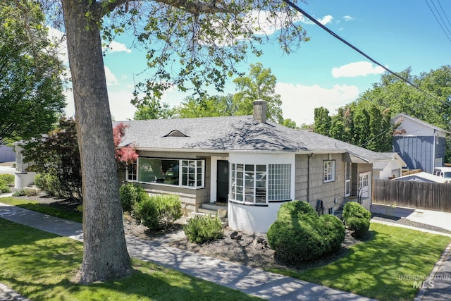 view of front of property with a chimney, roof with shingles, a front lawn, and fence