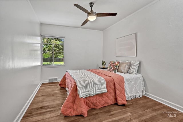 bedroom with visible vents, crown molding, baseboards, and wood finished floors