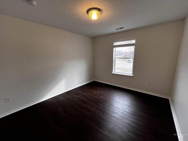 unfurnished room with baseboards, a textured ceiling, visible vents, and dark wood-type flooring