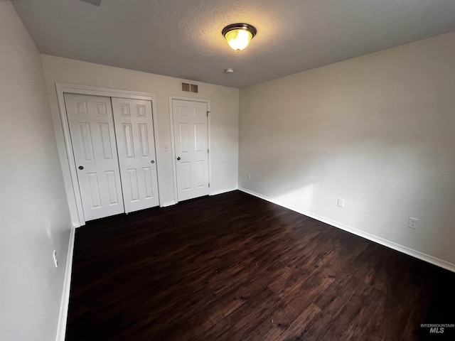 unfurnished bedroom featuring a textured ceiling, dark wood-style flooring, visible vents, baseboards, and a closet