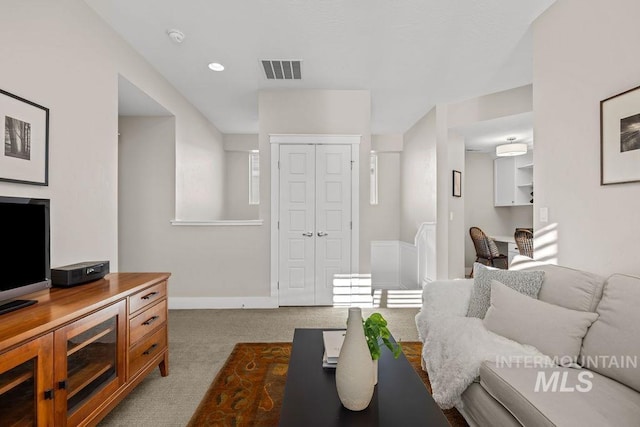 living area featuring baseboards, visible vents, and light colored carpet