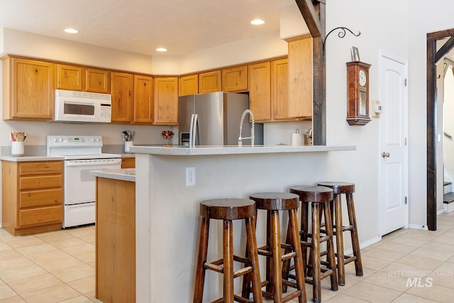 kitchen with white appliances, a breakfast bar, light tile patterned flooring, light countertops, and recessed lighting