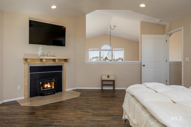 bedroom with lofted ceiling, a lit fireplace, wood finished floors, and baseboards