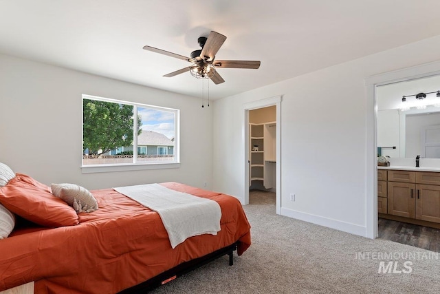 bedroom featuring light carpet, a sink, baseboards, a walk in closet, and ensuite bath