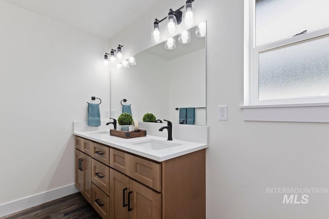 full bath with double vanity, wood finished floors, a sink, and baseboards