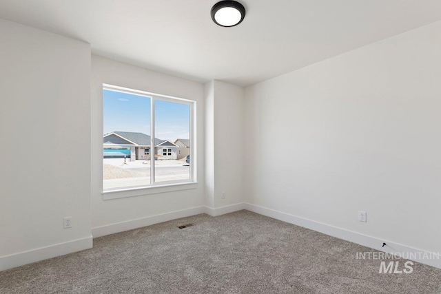 spare room with carpet floors, visible vents, and baseboards