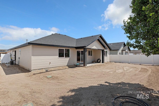 rear view of house with central AC unit, roof with shingles, and fence