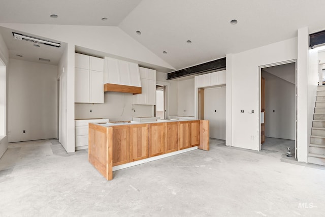 kitchen with white cabinets, premium range hood, a kitchen island with sink, and vaulted ceiling