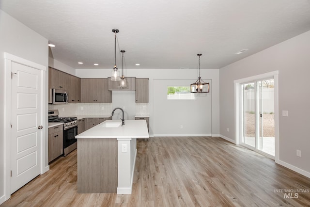 kitchen with a center island with sink, decorative light fixtures, light hardwood / wood-style floors, and appliances with stainless steel finishes