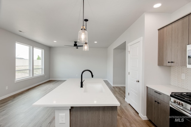 kitchen with a kitchen island with sink, sink, pendant lighting, stainless steel gas stove, and light hardwood / wood-style floors