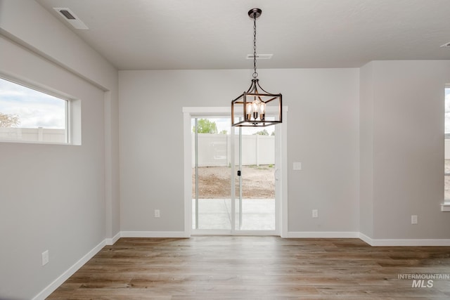 unfurnished dining area with plenty of natural light, a chandelier, and hardwood / wood-style flooring