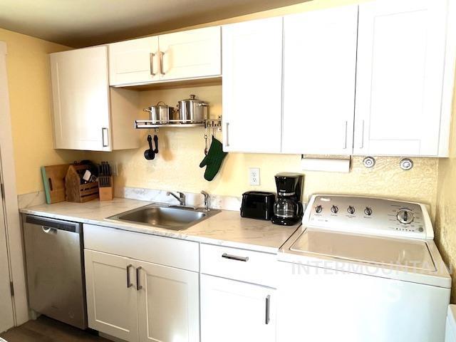 kitchen featuring washer / clothes dryer, dishwasher, sink, and white cabinetry