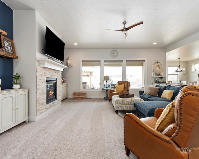 carpeted living room featuring a stone fireplace, ceiling fan with notable chandelier, a healthy amount of sunlight, and recessed lighting