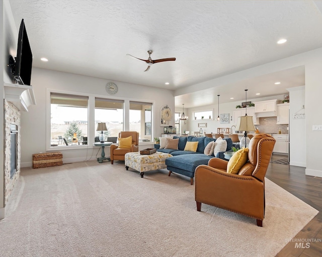 living area featuring a stone fireplace, recessed lighting, baseboards, and a textured ceiling