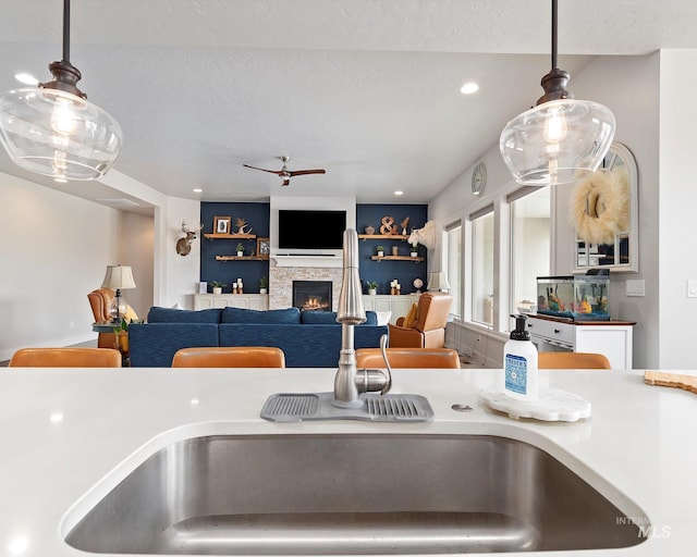 kitchen featuring a sink, a ceiling fan, a fireplace, and hanging light fixtures