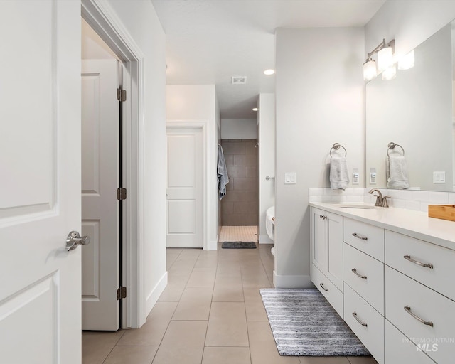 bathroom with toilet, tiled shower, tile patterned flooring, baseboards, and vanity