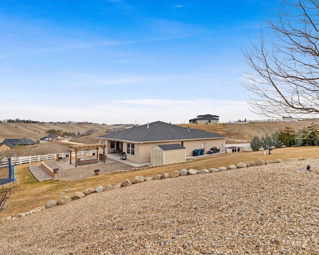 rear view of house with fence, stucco siding, an outdoor structure, a storage shed, and a patio area