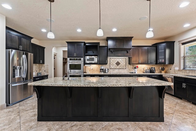 4315 N Nuova Ave, Meridian, ID 83646 - kitchen featuring appliances with stainless steel finishes, a kitchen island with sink, decorative light fixtures, and light stone counters