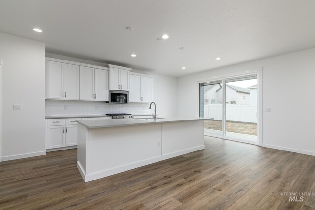 kitchen with dark wood-style floors, white cabinets, decorative backsplash, and stainless steel microwave