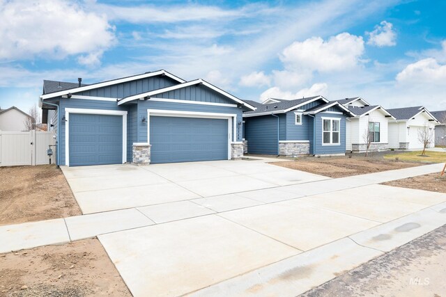 view of front of property with stone siding, fence, a garage, board and batten siding, and driveway