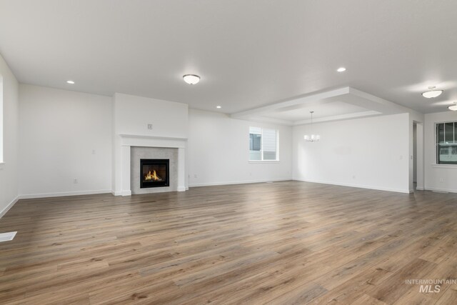 unfurnished living room featuring an inviting chandelier, recessed lighting, a glass covered fireplace, and wood finished floors