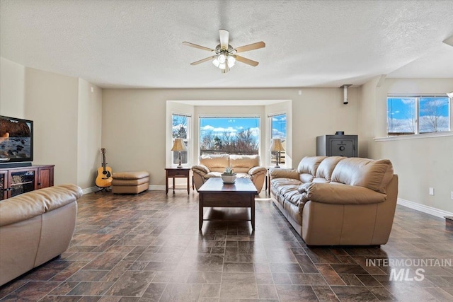 living room featuring stone finish flooring, a textured ceiling, baseboards, and a ceiling fan