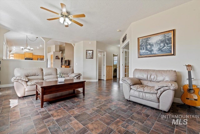 living area featuring baseboards, washer / clothes dryer, stone finish flooring, a textured ceiling, and ceiling fan with notable chandelier