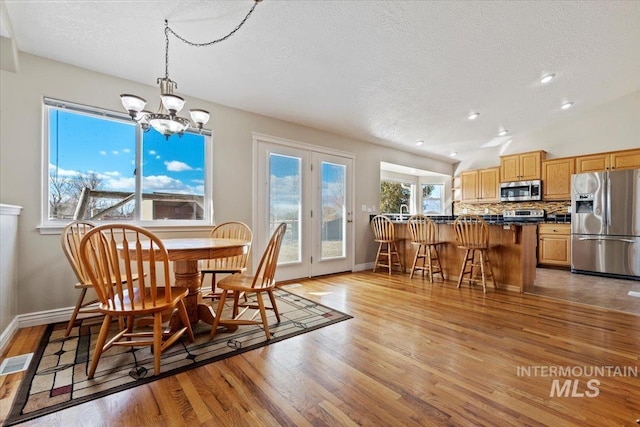 dining room with baseboards, light wood-style flooring, visible vents, and a textured ceiling