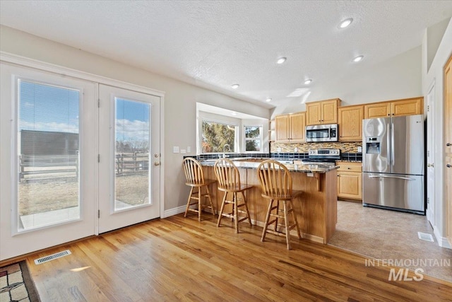 kitchen featuring visible vents, backsplash, appliances with stainless steel finishes, vaulted ceiling, and a kitchen bar