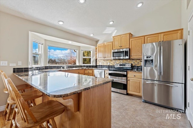 kitchen with a breakfast bar area, stainless steel appliances, backsplash, dark stone countertops, and a peninsula