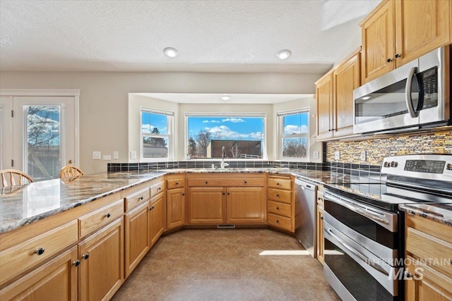 kitchen with light stone counters, stainless steel appliances, tasteful backsplash, a sink, and a textured ceiling