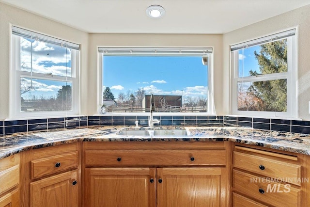 kitchen featuring dark stone counters, a sink, a wealth of natural light, and decorative backsplash