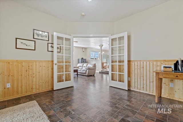 interior space with french doors, a wainscoted wall, stone finish floor, and wooden walls