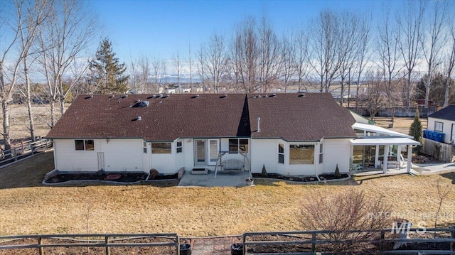 rear view of house with a fenced front yard, roof with shingles, a patio, and a lawn