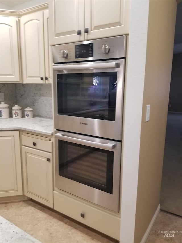 kitchen featuring light tile patterned flooring, stainless steel double oven, light stone countertops, and decorative backsplash