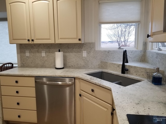 kitchen with sink, light stone counters, stainless steel dishwasher, cream cabinetry, and backsplash