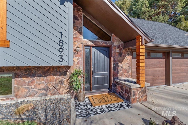 property entrance featuring a garage, stone siding, and roof with shingles