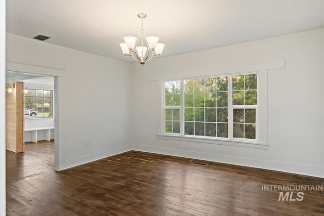 unfurnished room with a chandelier, visible vents, wood finished floors, and baseboards