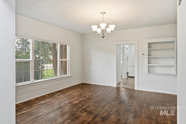 empty room with wood-type flooring, a notable chandelier, built in features, and baseboards