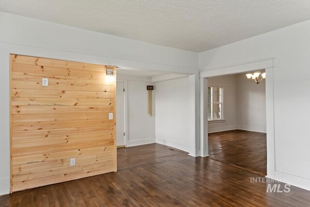 empty room with a textured ceiling, a notable chandelier, wood finished floors, and baseboards